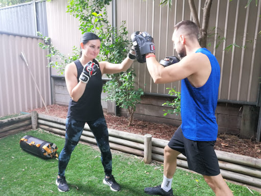 Client and personal trainer doing boxing pad work together in the garden