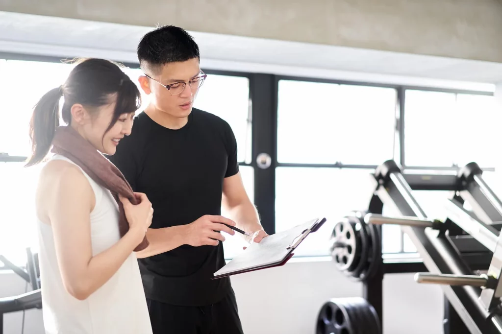 one asian man and one asian woman looking at a clipboard while inside a gym